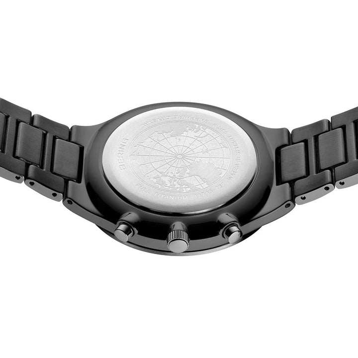 De achterkant van het Bering horloge, model 11743-727, heeft een metalen band en een ronde zilveren kastbodem gegraveerd met een wereldkaart en tekst. Het bevat twee pushers en een kroon aan de zijkant, wat het elegante titanium design benadrukt.