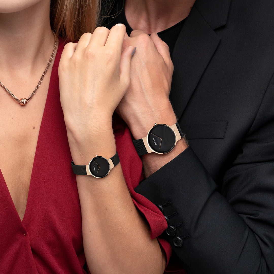 Een vrouw in een rode jurk en een man in een zwart pak showen hun bijpassende Bering 14539-166 horloges. Het minimalistische ronde design en de roestvrijstalen kasten complementeren haar ketting met een ronde hanger perfect.