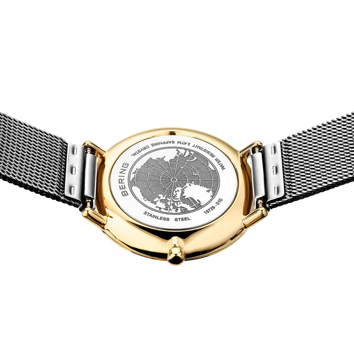 Op de afbeelding is de onderkant van een Bering Dameshorloge 15729-010 te zien met een kast van roestvrij staal van goud en zilver, een gegraveerde kaart en een strakke, zilveren mesh-band met de inscriptie BERING, STAINLESS STEEL en plaatsnamen zoals ISLANDS, PLAINS, LYKE. Dit alles toont de precisie van Quartz-technologie.
