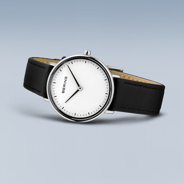 Het Bering 15729-404 Dameshorloge heeft een blauwe achtergrond en straalt minimalistische elegantie uit met zijn witte wijzerplaat, dunne zwarte wijzers, zwarte leren band, strakke zilveren kast, Saffierglas en Quartz-uurwerk.