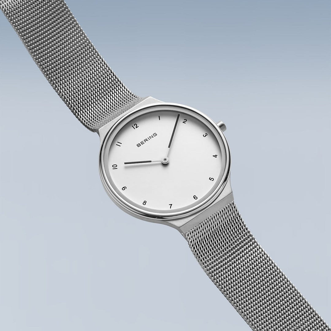 Het Bering dameshorloge model 18434-004 heeft een minimalistisch design met een gradiënt blauwe achtergrond, witte wijzerplaat, eenvoudige zwarte uurmarkeringen en dunne wijzers, allemaal beschermd door duurzaam saffierglas. Het bevat een zilveren mesh band en is van het bekende merk Bering.