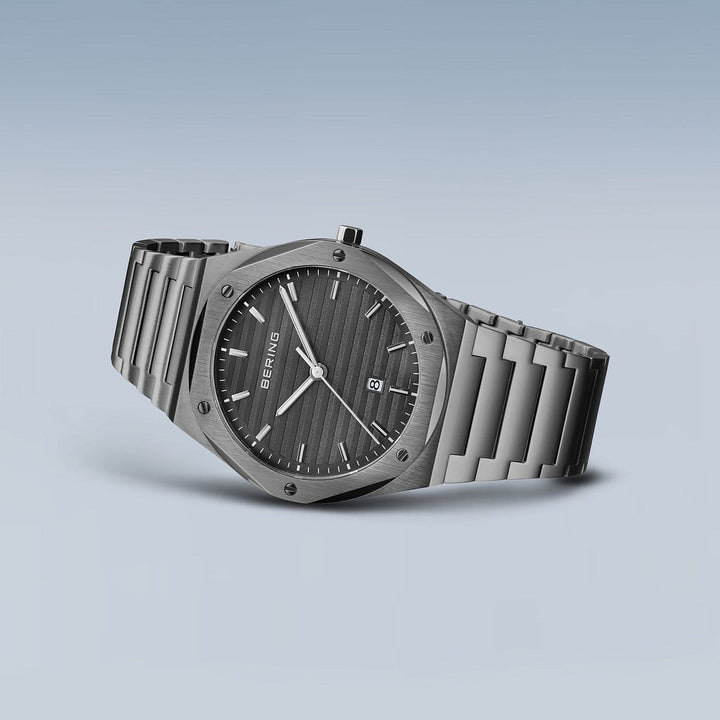 Het Bering herenhorloge 19742-777, met een strakke roestvrijstalen kast en metalen band, benadrukt het minimalistische ontwerp met een zwarte gestructureerde wijzerplaat, zilveren uurmarkeringen, twee zilveren wijzers en een datumaanduiding op een grijze achtergrond met duurzaam saffierglas.