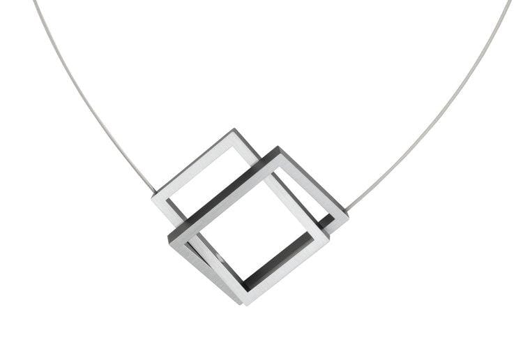 De Collier Twee rechthoeken in elkaar Zwart C30Z van CLIC Creations toont twee in elkaar grijpende zilveren vierkante frames in een hoek op een dunne draad. Met een magnetische sluiting combineert het moderne elegantie en bruikbaarheid tegen een effen witte achtergrond.