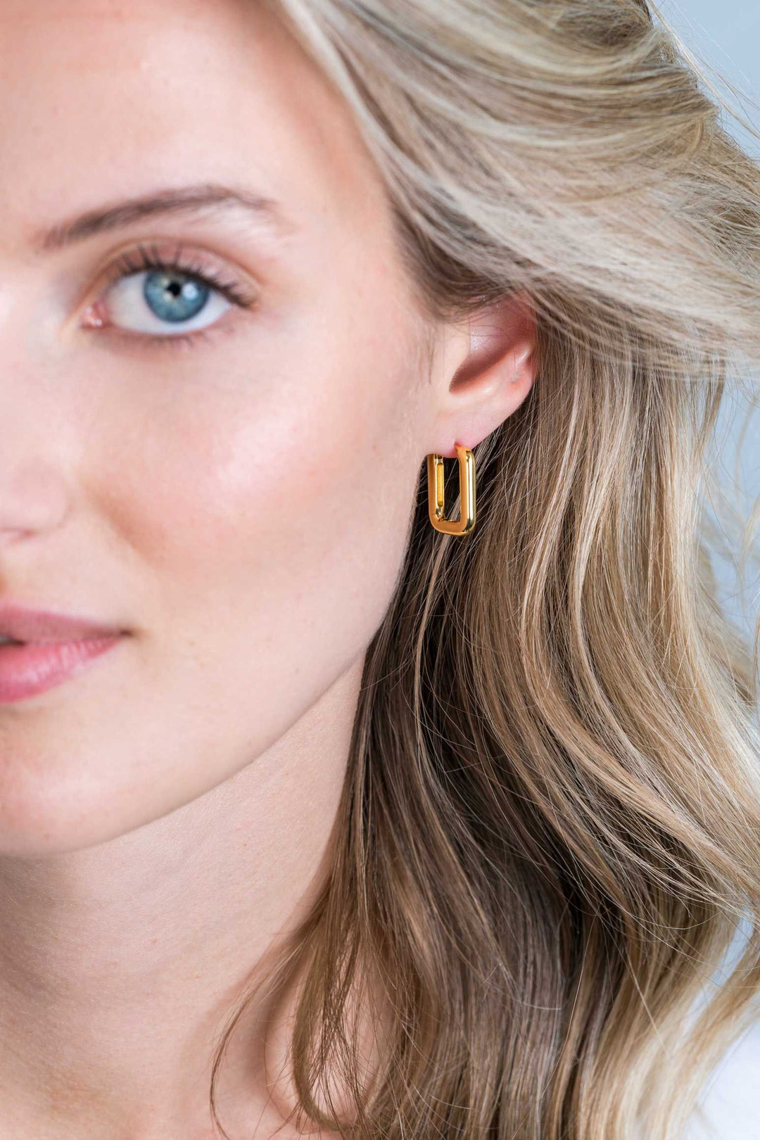 Close-up van een vrouw met een lichte huid en blond haar, die Zinzi Oorbellen Gold Plated Zio2221 G oorbellen draagt. De focus ligt op haar blauwe oog en de vergulde oorbel, aangevuld met neutrale make-up en zachte golven in haar haar.
