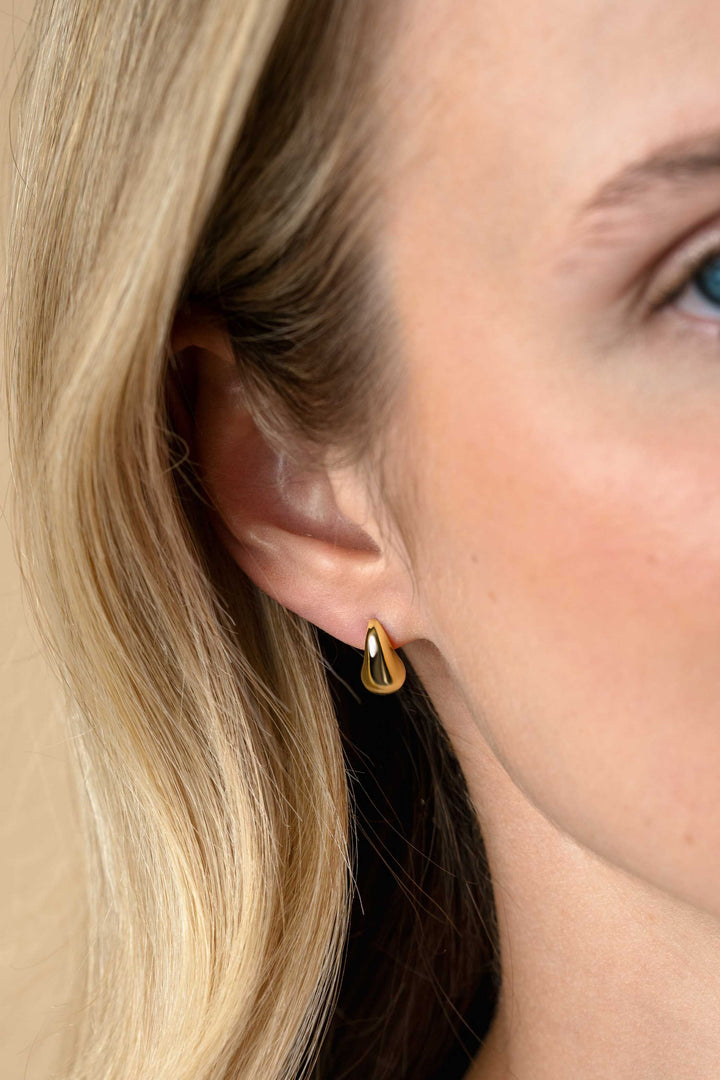 Close-up van het oor van een vrouw met een Zinzi Oorbellen Zilver verguld ZIO2636G traanvormige oorbel. Haar blonde haar is weggestopt achter haar oor, met slechts een deel van haar gezicht zichtbaar tegen een neutrale achtergrond. Merk: Zinzi.
