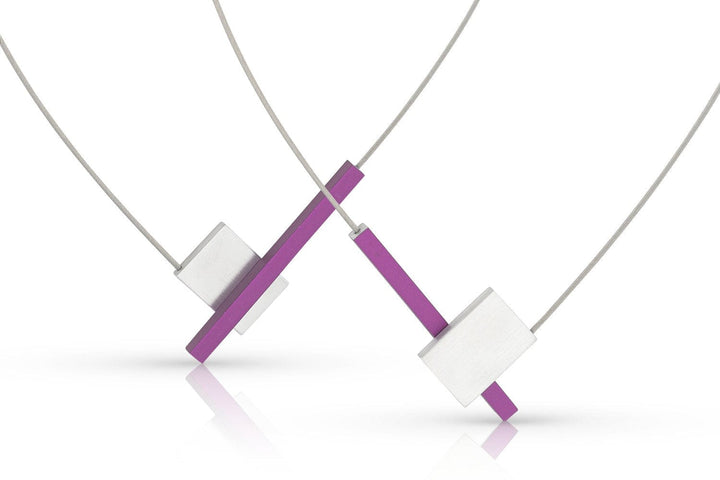 De CLIC Creations Collier V-vorm met staafje C261P bestaat uit twee moderne kettingen met geometrische ontwerpen, die handgemaakt vakmanschap in Nederland laten zien. Ze omvatten een rechthoekig paars segment dat kruist met zilveren vierkanten, opgehangen aan dunne koorden voor een minimalistische look.