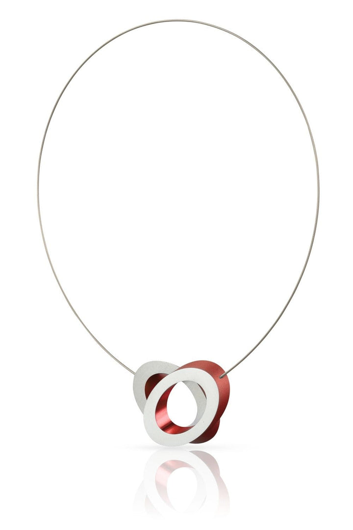 De Collier Ovalen op elkaar Rood C70R van CLIC Creations is een strakke ketting met een dunne draad en een hanger van drie onderling verbonden geometrische ringen, twee zilveren en één rode, voor een moderne, minimalistische look. Handgemaakt in Nederland, heeft een eenvoudige magnetische sluiting en reflecteert elegant hieronder.