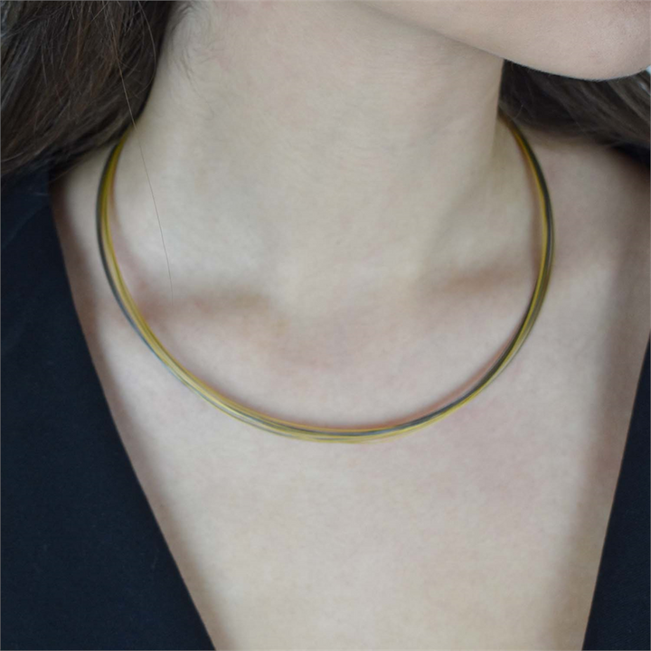 Een close-up toont een persoon die de Boccia Titanium Lengte Collier Bicolor staal 0859-03 draagt, een slanke tweekleurige choker halsketting van Boccia, gecombineerd met een zwart topje en met nadruk op de hals en het sleutelbeen.