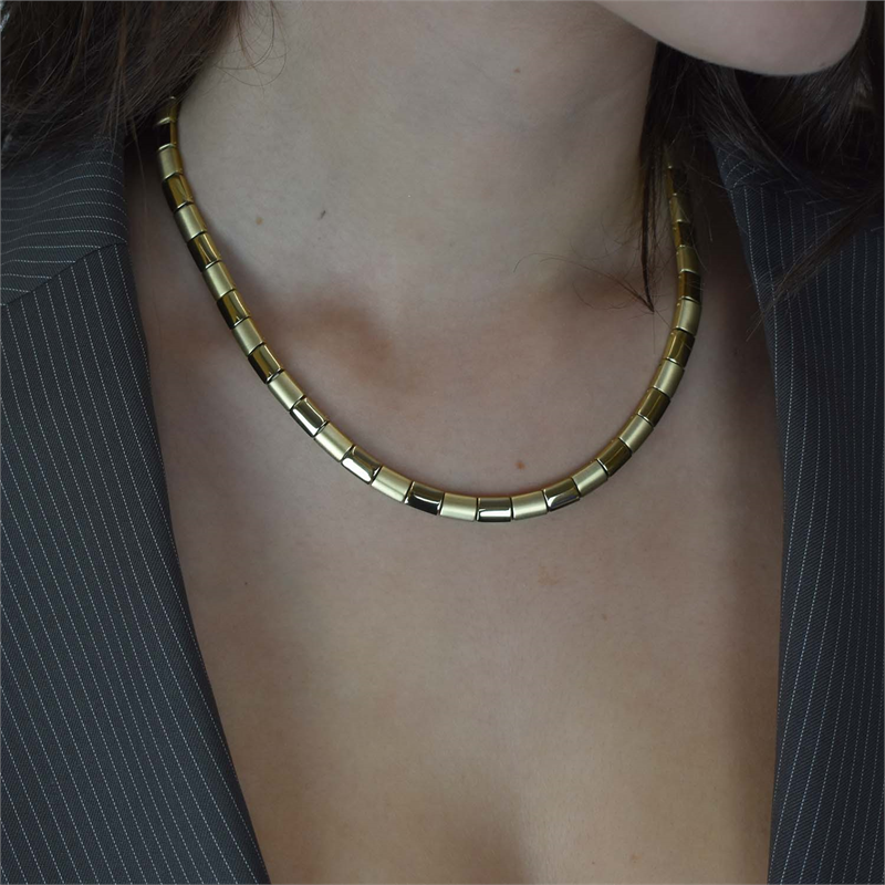Een vrouw in een krijtstreepjasje draagt de Boccia Titanium Collier gp 0812-11 van Boccia, met rechthoekige schakels die het elegante ontwerp van haar schouders tot haar kin benadrukken.