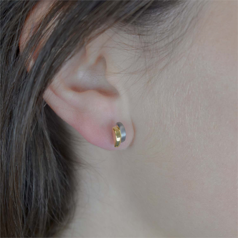 Close-up van het oor van een persoon met steil bruin haar, die Boccia Titanium Oorstekers Bicolor 0552-03 draagt: kleine, moderne oorbellen in zilver- en goudtinten van Boccia.