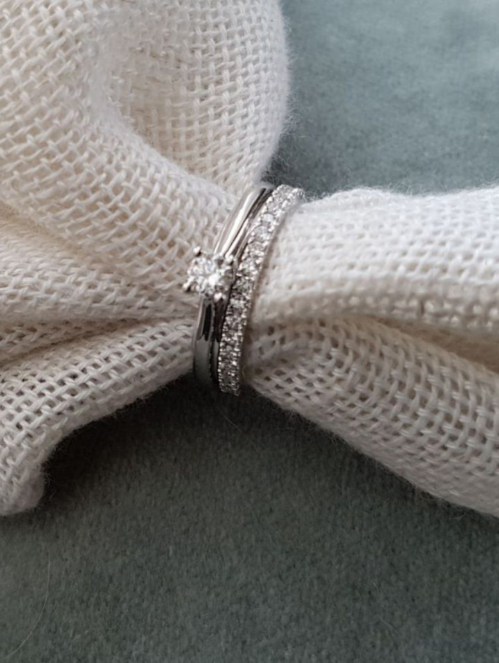 De Witgouden Ring met Briljant Diamant - Subtiele Elegantie voor Elke Gelegenheid 0.25 crt. van Excellent Jewelry ligt samen met een bijpassende diamanten band op wit textiel, tegen een zachte grijze achtergrond.
