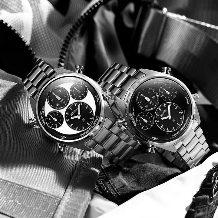 Twee Seiko Prospex SFJ003P1 chronograafhorloges van roestvrij staal, met zwarte wijzerplaten en subdials, liggen op een gestructureerde stof. Eén heeft een contrasterende witte wijzerplaat. Beide hebben schakelarmbanden, die het klassieke Seiko-ontwerp laten zien.