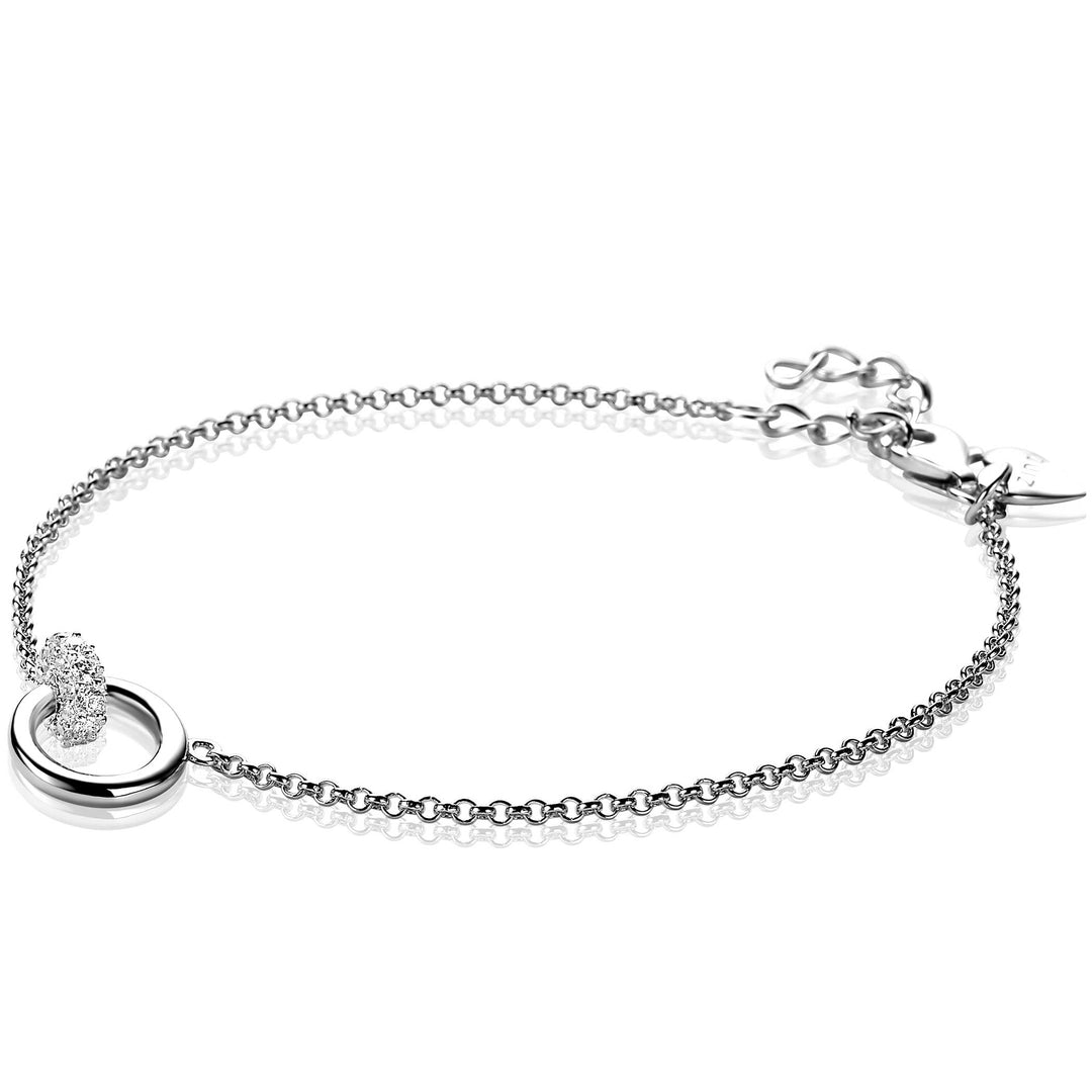 De Zinzi Armband Zilver Zia1830 benadrukt een elegant cirkelvormig lusontwerp met een delicaat getextureerd accent tegen een witte achtergrond. Het bevat een verstelbare sluiting met extra schakels voor perfecte maataanpassing.