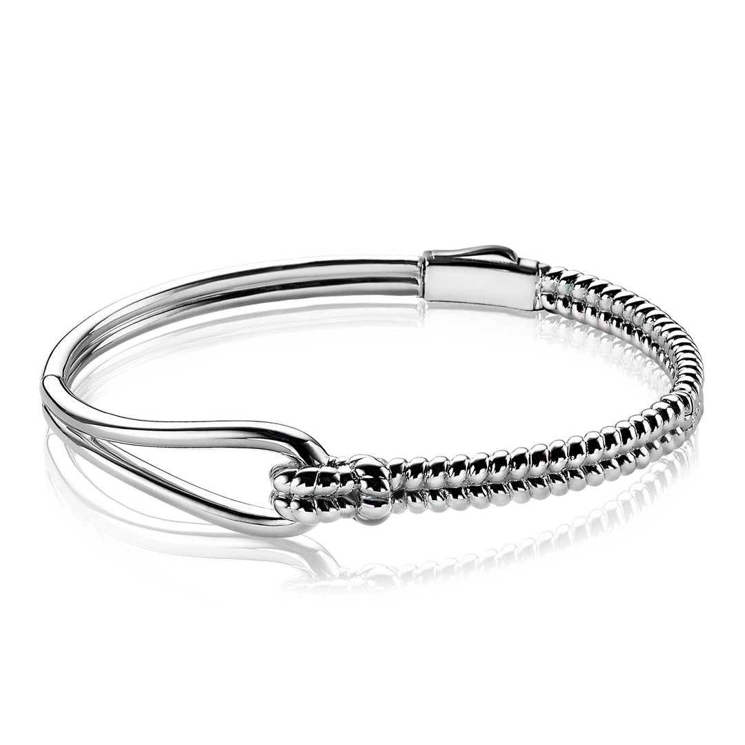 De Zinzi Armband Zilver Mva9 heeft een strak design met een gladde helft en een opgerolde helft. Het heeft een minimalistische haaksluiting, elegant gepresenteerd op een reflecterend wit oppervlak, wat de glanzende afwerking en ingewikkelde details van het bekende merk Zinzi benadrukt.